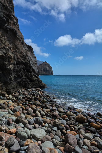 Foto Vertical perspective of the ocean waves washing ashore near towering dark rock formations under a partly cloudy sky