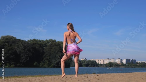 Smiling Tanned Woman In Summer Dress Posing Near A Peaceful River. Dancing And Relaxing In A Beautiful Outdoor Setting.