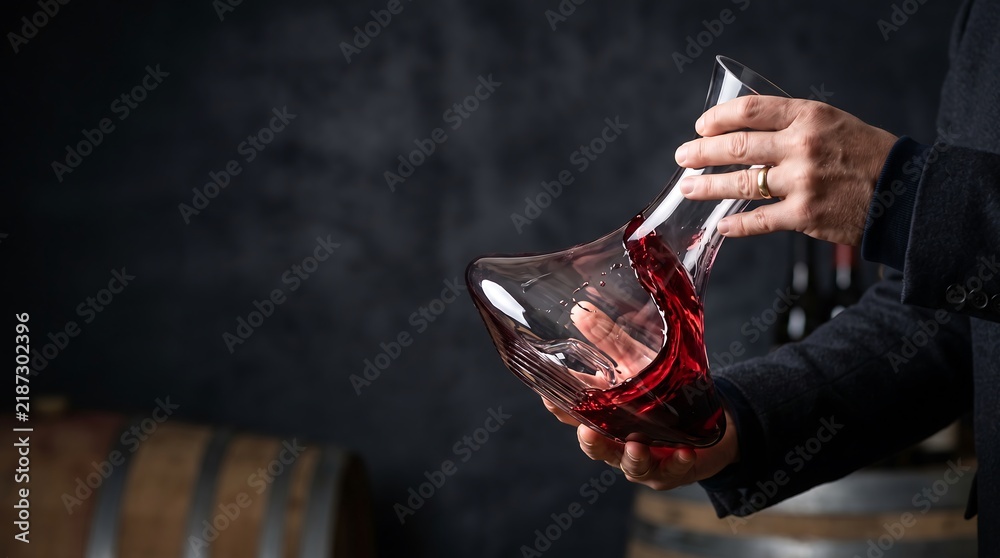 Obraz premium Sommelier pouring red wine from a glass decanter into a glass in a dark cellar