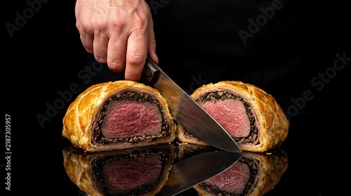 Chef slicing beef wellington with a knife on a black background