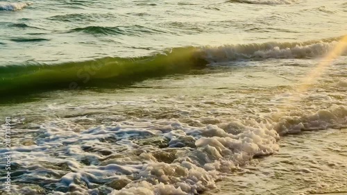 Close up slow motion of gentle ocean wave foam on wet sand at golden hour