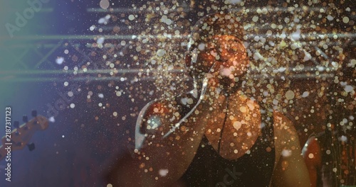 Fotografie Singing vocalist in dark tank top performing on club stage, holding mic, guitar
