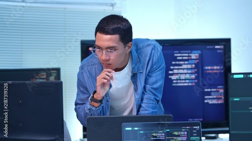 Focused programmer analyzing code in high tech it workspace with multiple monitors displaying data and graphs