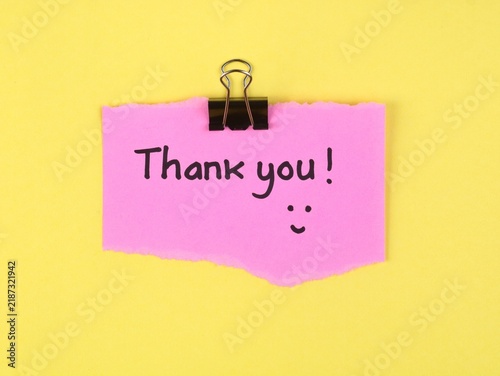 Fotografie Handwritten Thank you note with a happy face on a torn pink paper scrap, held by a black binder clip and pinned to a vibrant yellow background