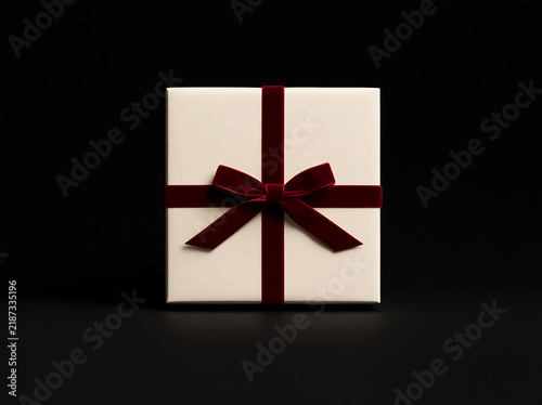 Luxury holiday present packaging. Cream square gift box with deep red velvet ribbon and bow isolated  on a black background. 