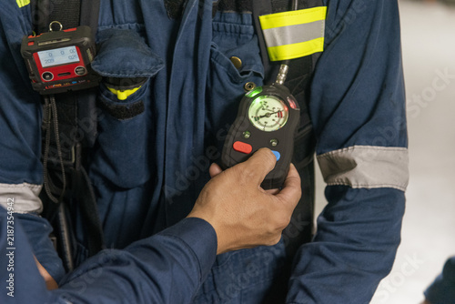 Fotografie Detailed view of shipboard emergency response equipment, showing an SCBA air pressure gauge and personal gas detector secured to a crew member's protective clothing during safety training