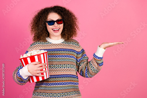 Bild auf Leinwand Happy young woman wearing 3D glasses holding popcorn and gesturing on pink backg