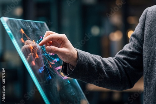 Businessman interacting with a futuristic transparent digital screen displaying data networks and analytics in a modern office