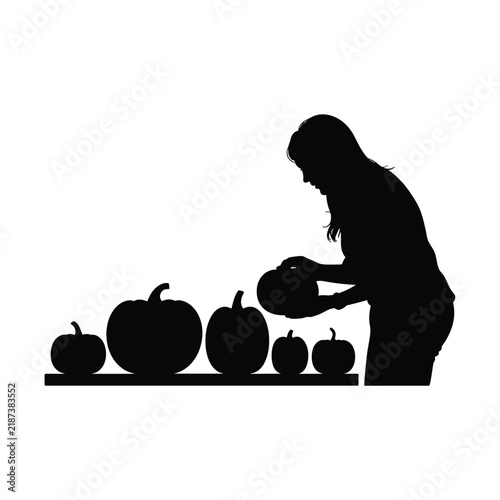 Woman silhouette arranging fresh ripe pumpkins on wooden shelf for autumn market display