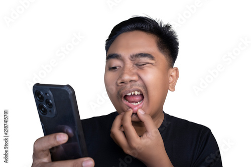 Painful and wincing Indonesian man wearing a black t-shirt looking at his mobile phone while holding his lower lip and mouth with his hands