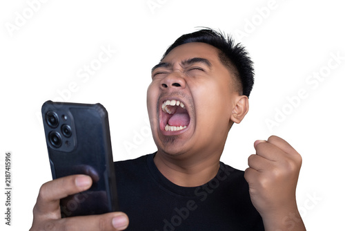 Overjoyed and ecstatic Indonesian man wearing a black t-shirt looking at his mobile phone while pumping his fist and screaming loudly in celebration against a white background.