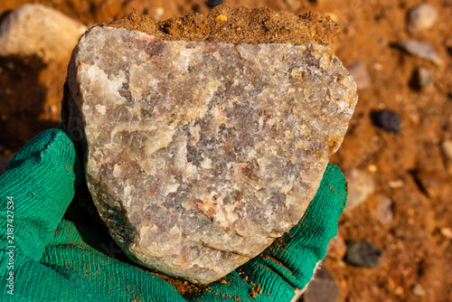 Photography Close-up of a raw vein quartz boulder held in a gloved hand, showcasing a natura