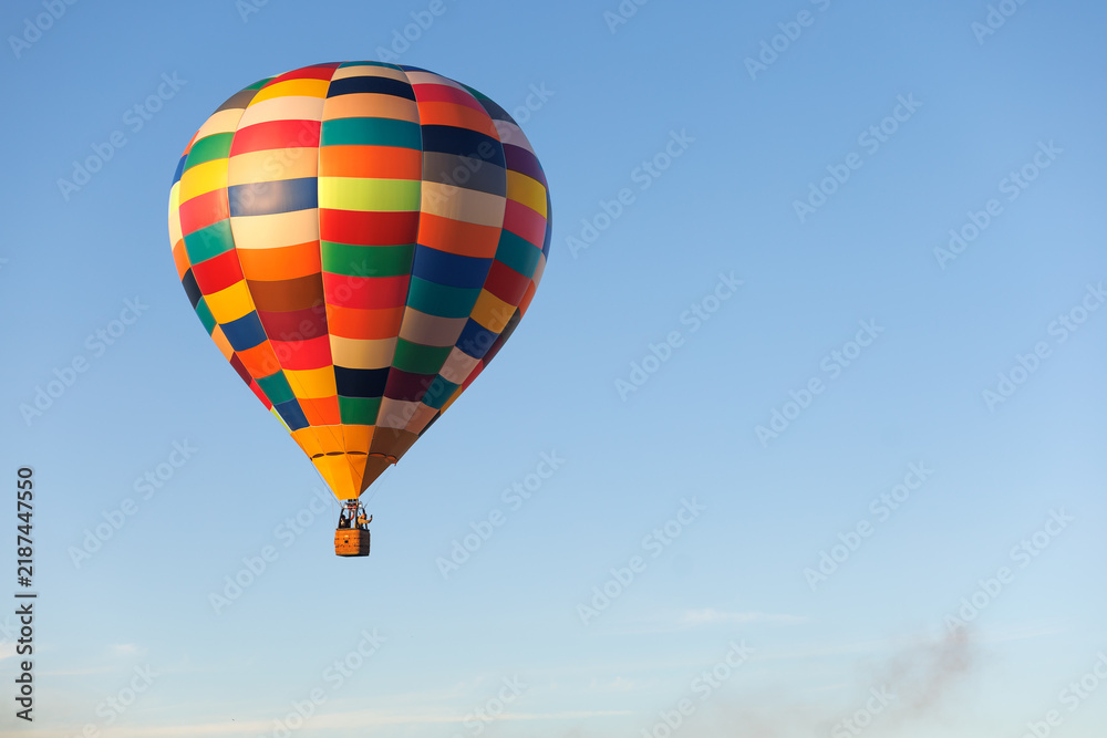 Fototapeta premium Colorful hot air balloon drifts across an open blue sky with extensive copy space. Concept of peaceful flight, freedom, exploration, balloon tourism and adventure travel.