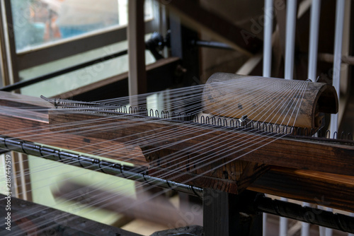 Close-up of a wooden loom reed with white warp threads strung through its metal teeth, Kyushu region, Chikugo, Japan