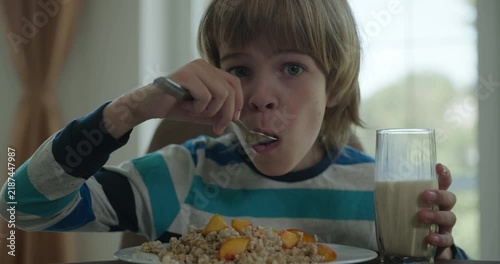 Caucasian kid boy eat oatmeal and peach in dining room. Child eating food. 4K 10-bit