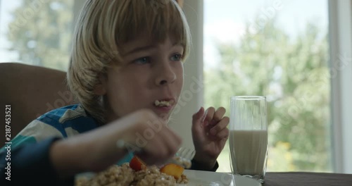Caucasian kid boy eat oatmeal and peach in dining room. Child eating food. 4K 10-bit