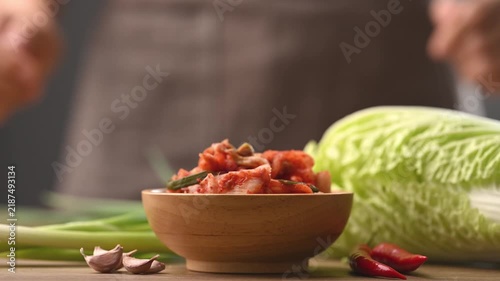 Woman hand putting down a wooden bowl of Kimchi Napa cabbage on a table, Korean side dish (Banchan)