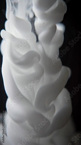 Macro shot of thick white acrylic ink dropping into water and swirling gracefully against a pure black background