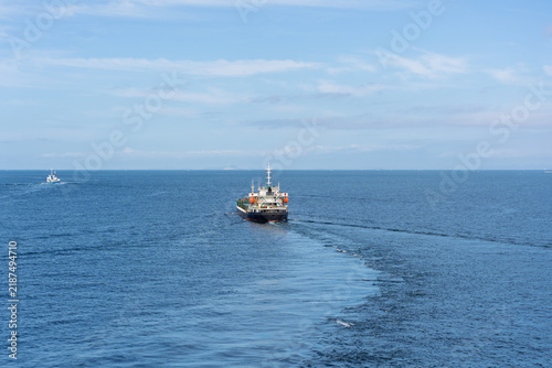 Small cargo ship sails calm blue water into open sea on sunny day