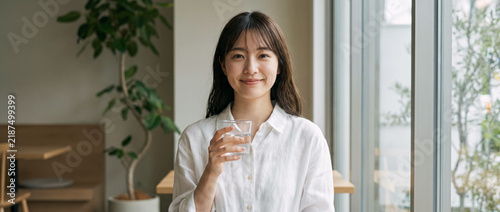 Portrait of a smiling young Japanese woman holding a glass of water in a cafe