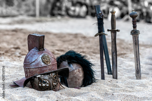 Foto Cascos de gladiador romano con crestas y varias espadas clavadas en suelo arenoso al aire libre durante una recreación histórica