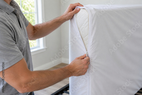 Hands closing a zippered encasement around a mattress corner