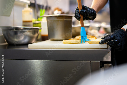 Obraz na plátně A chef in black gloves uses a blue silicone brush to baste sliced bread on a cutting board in a professional kitchen