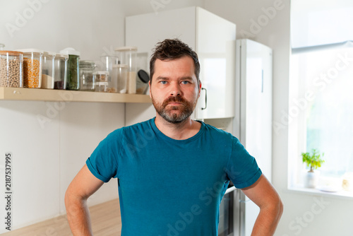 Foto A man of Caucasian appearance in a blue T-shirt stands in a white kitchen near t