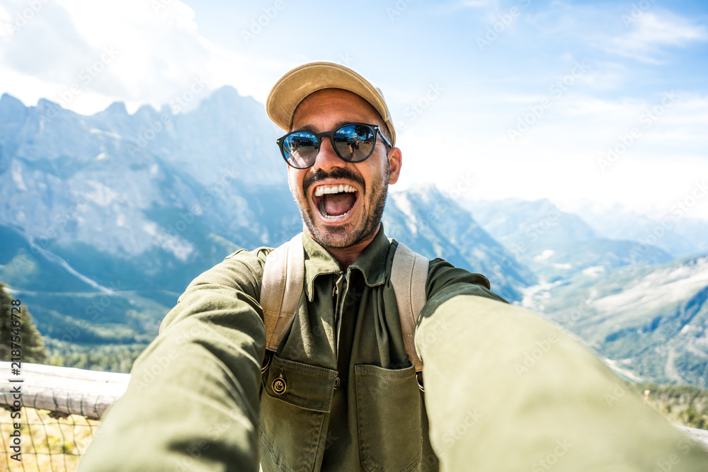 Fototapeta premium Young hiker man taking selfie portrait on the top of mountain - Smiling man enjoying summer vacations with italian alps on background