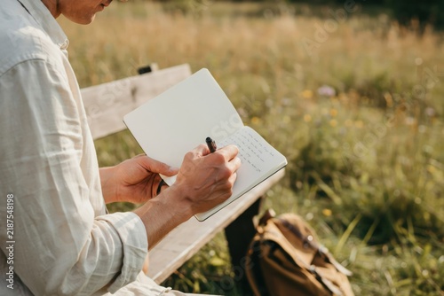 Man writing in a notebook while sitting on a wooden bench in a meadow