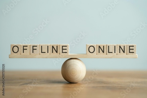 Wooden blocks with the words offline and online balancing on a wooden scale