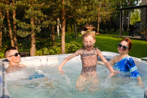 Fotografie Family enjoys time in hot tub on sunny day outdoors with trees and a green lawn