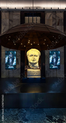 A large classical stone sculpture head displayed under a suspended dome structure with embedded lights in a museum.