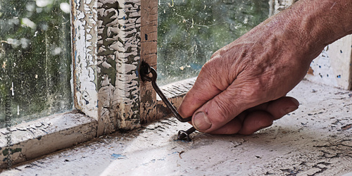 Bild auf Leinwand Weathered hand of an elderly person securing a rusted metal hook to hold up an o