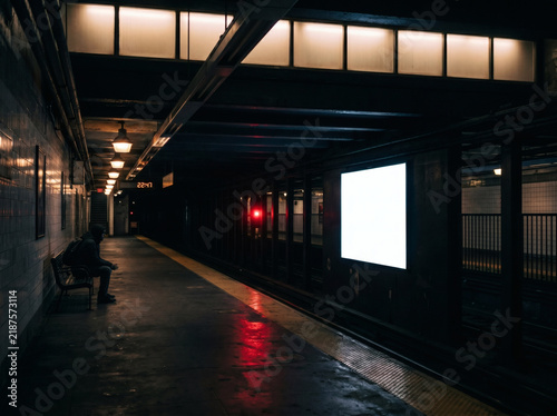 Solitary figure waits on illuminated subway platform near glowing advertisement screen