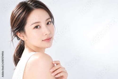 Fototapeta 白背景で肩に手を添えて振り返る若い日本人女性の清潔感ある美容ポートレート