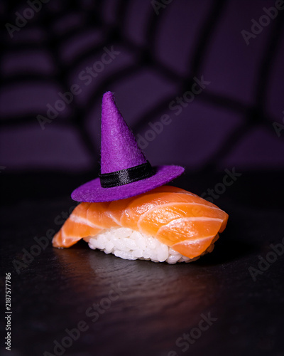 Halloween sushi on dark background. Salmon nigiri with purple witch hat on top. Creative party food. Spooky, scary, fun, bewitched, beautiful, funny, stylish. Japanese bar, restaurant holiday menu