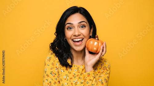 Young woman holding a small pumpkin against a vibrant yellow background