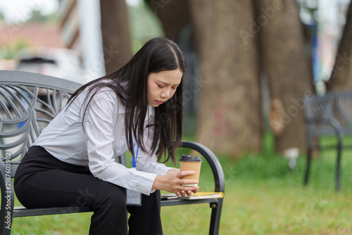 Stressed Asian businesswoman sitting on bench with coffee during work break