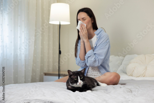 Fotografía Adult woman experiencing sneezing and allergy symptoms near a domestic cat, repr