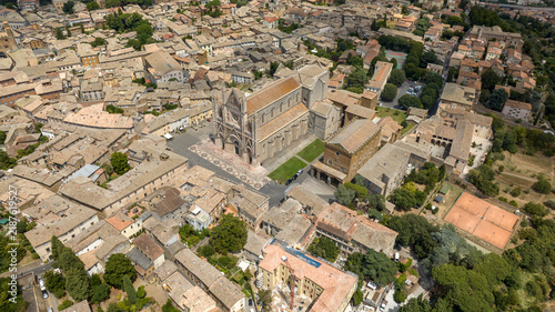 Aerial view showcases the stunning Orvieto Cathedral rising above the historic Italian town, highlighting medieval Gothic architecture surrounded by traditional terracotta rooftops and streets.