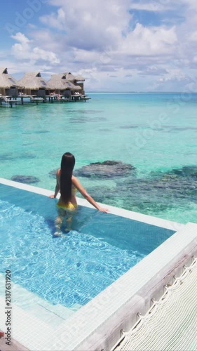 Luxury resort travel vacation destination idyllic overwater bungalow villa woman relaxing by infinity pool. Social media influencer traveler luxurious lifestyle. Raw vertical video of real woman.