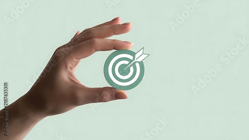 A hand holding a circular target against a soft green background, representing business goals, and strategic planning, for success and achievement