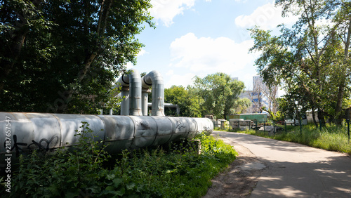Large industrial heating pipes and urban utility infrastructure located in a green city environment, representing energy systems, district heating networks and municipal engineering