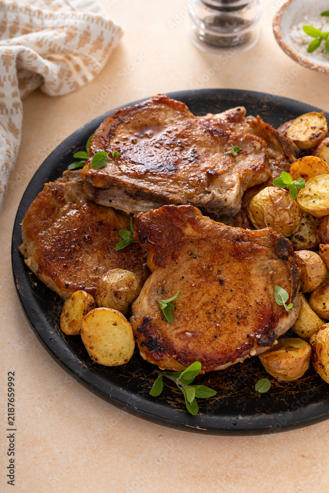 Obraz premium Pork chops on a bone grilled or sauteed served with roasted potatoes on a plate