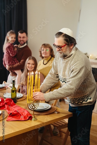 Fotografie Senior man lighting candles on hanukkah menorah at home
