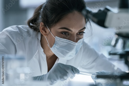 Lab technician examining sample under microscope in laboratory