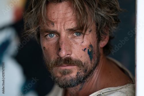 Painter with paint-smeared face looking intently at canvas
