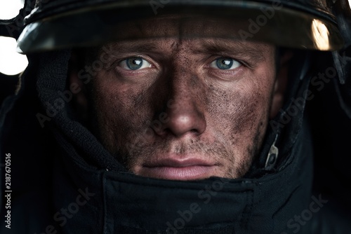 Dimly lit close-up of firefighter with soot-covered face and helmet in protective gear