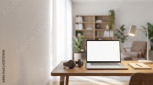 Silver laptop with blank white screen sits on wooden desk featuring modern headphones and a bright metallic desk lamp